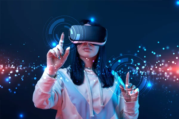 Woman in virtual reality headset pointing with fingers at glowing cyber illustration on dark background — Stock Photo
