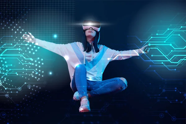 KYIV, UKRAINE - APRIL 5, 2019: Young woman in virtual reality headset with joystick and outstretched hands flying in air among glowing data illustration on dark background — Stock Photo