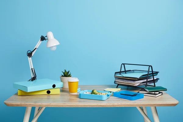 Workspace with lunch box and coffee to go on wooden table on blue background — Stock Photo