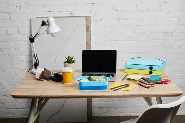 Boîte à lunch avec de délicieux aliments sur le lieu de travail avec ordinateur portable et papiers sur table en bois sur fond blanc, éditorial illustratif — Photo de stock