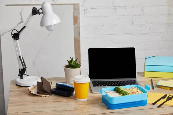 Lonchera de plástico azul con comida saludable en mesa de madera con portátil y suculenta sobre fondo blanco, editorial ilustrativa - foto de stock