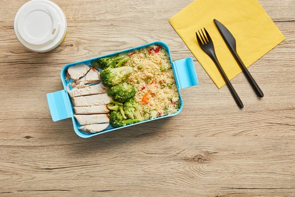 Vue du dessus de la boîte à lunch saine avec poulet cuit, brocoli, riz et café dans une tasse en plastique sur une table en bois — Photo de stock