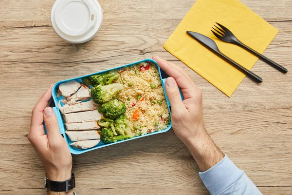 Abgeschnittene Ansicht eines Mannes, der am Tisch sitzt und eine Lunchbox mit gesundem und schmackhaftem Essen in der Hand hält — Stockfoto