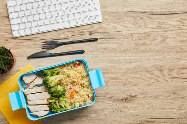 Vue du dessus de la boîte à lunch avec riz, brocoli et poulet près du clavier d'ordinateur sur une table en bois — Photo de stock