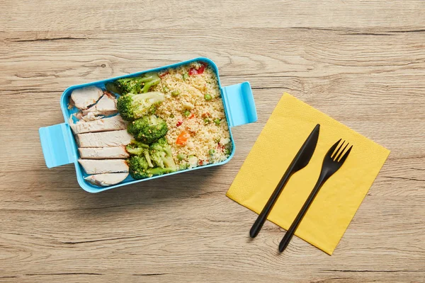 Vista superior de la lonchera de plástico con risotto, pollo y brócoli sobre mesa de madera - foto de stock