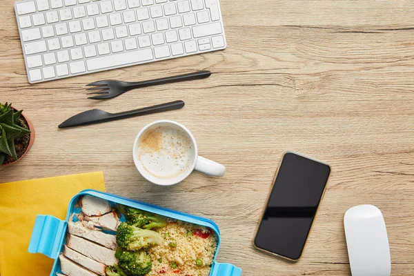 Vista superior da lancheira com refeição saborosa, bebida quente e dispositivos digitais na mesa de madeira — Stock Photo