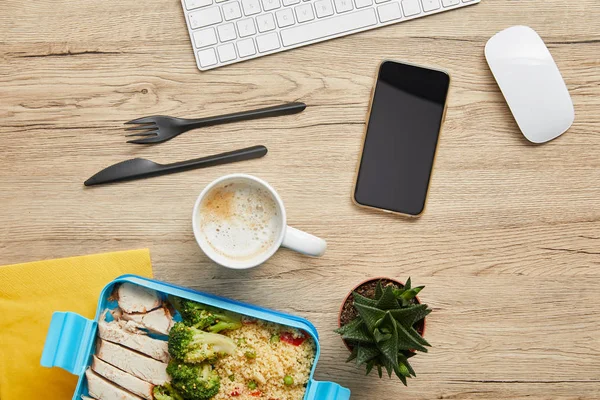 Vista superior da lancheira com deliciosa comida saudável, bebida quente e dispositivos digitais na mesa de madeira — Stock Photo