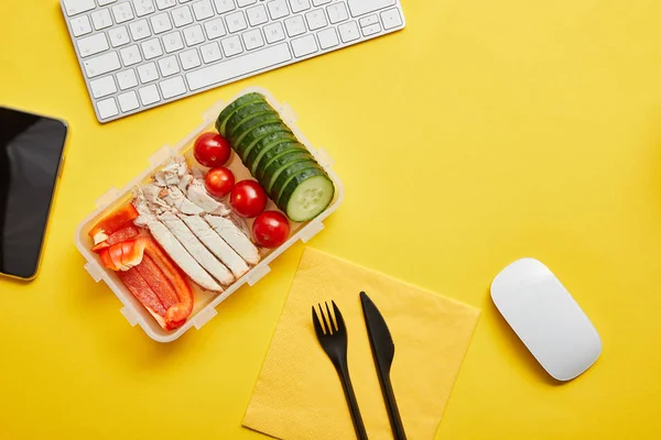 Vista dall'alto della scatola del pranzo con verdure e pollo su sfondo giallo con tastiera del computer — Foto stock