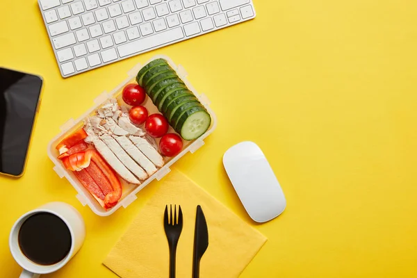 Vista superior de la lonchera con comida saludable y taza de café en el lugar de trabajo sobre fondo amarillo - foto de stock