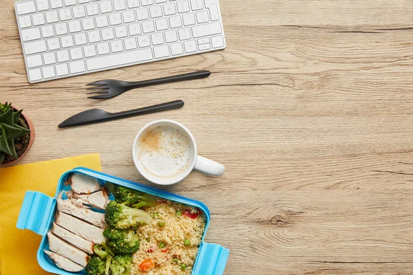 Top view of lunch box with risotto and cup of coffee at workspace on wooden table — Stock Photo