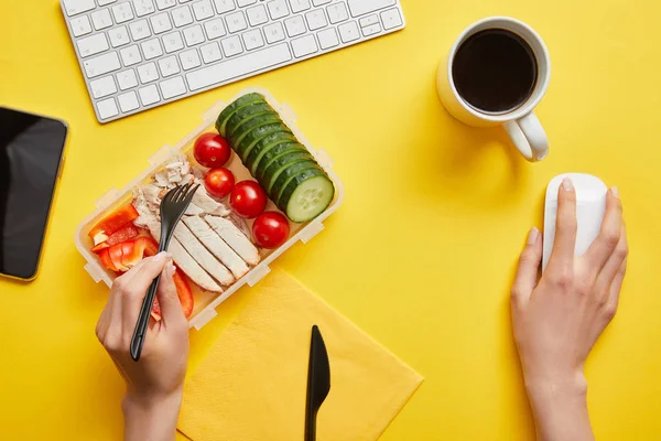 Vista ritagliata di donna mangiare delizioso pollo con verdure fresche e utilizzando il mouse del computer sul posto di lavoro — Foto stock