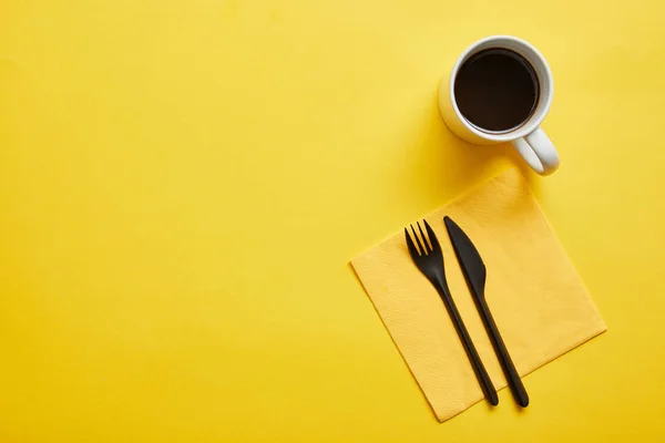 Vista superior de la taza de café caliente delicioso y tenedor y cuchillo desechables con servilleta amarilla sobre fondo amarillo - foto de stock