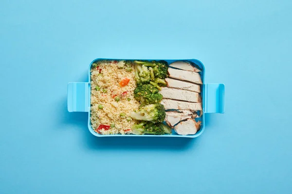 Vue du dessus de la boîte à lunch avec poulet savoureux, risotto et brocoli sur fond bleu — Photo de stock