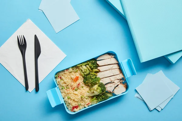 Top view of lunch box with tasty nutritious risotto, chicken and broccoli at workplace on blue background — Stock Photo