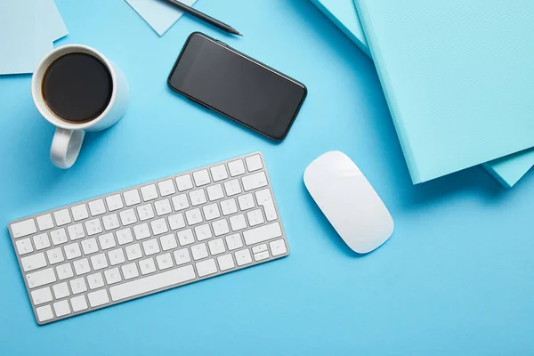 Vista superior del espacio de trabajo con dispositivos digitales, papeles y taza de café sobre fondo azul - foto de stock