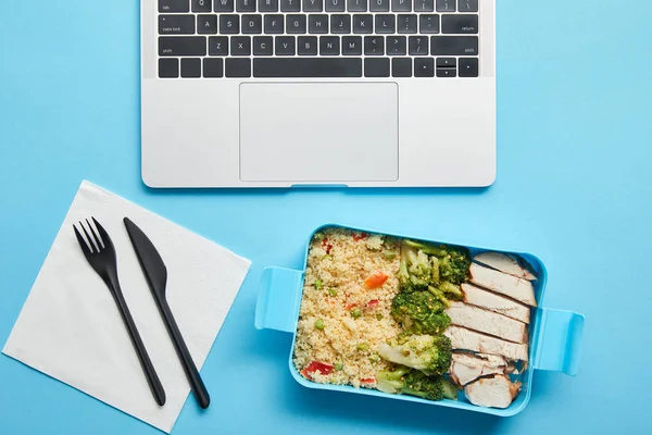 Top view of laptop keyboard and plastic lunch box with rice, broccoli and chicken on blue background, illustrative editorial — Stock Photo
