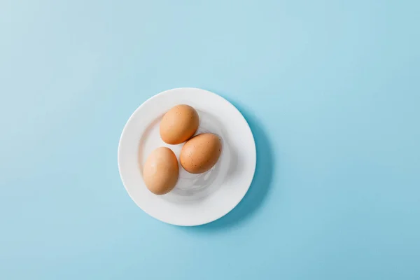 Vista dall'alto di uova fresche su piatto bianco su sfondo blu — Foto stock