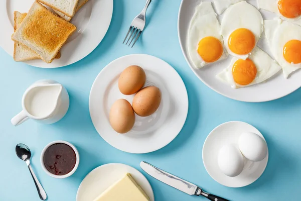 Vista superior de la mesa para el desayuno con tostadas y huevos fritos sobre fondo azul - foto de stock