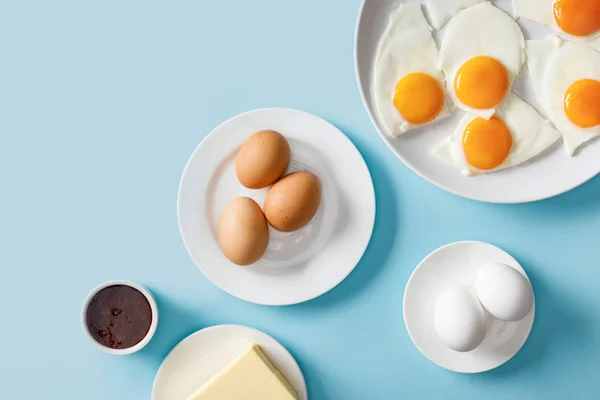 Вид сверху на вареные и жареные яйца, варенье и масло на синем фоне — стоковое фото