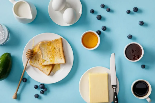 Vista superior del desayuno servido con aguacate y arándanos dispersos sobre fondo azul - foto de stock
