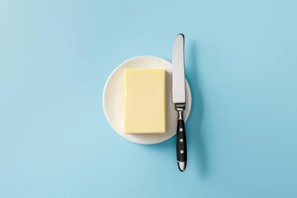 Top view of butter and knife on white plate on blue background — Stock Photo