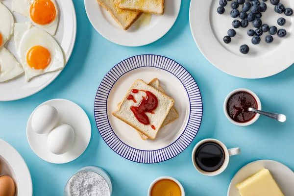 Vista dall'alto della tavola apparecchiata per colazione e brindisi con marmellata su piatti su fondo blu — Foto stock