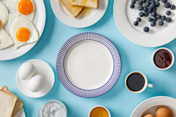 Vue du dessus du petit déjeuner servi avec assiette vide au milieu sur fond bleu — Photo de stock