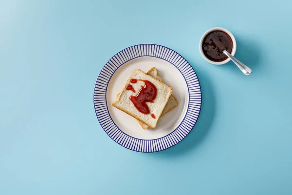 Top view of toasts on plate and spoon in bowl with jam on blue background — Stock Photo