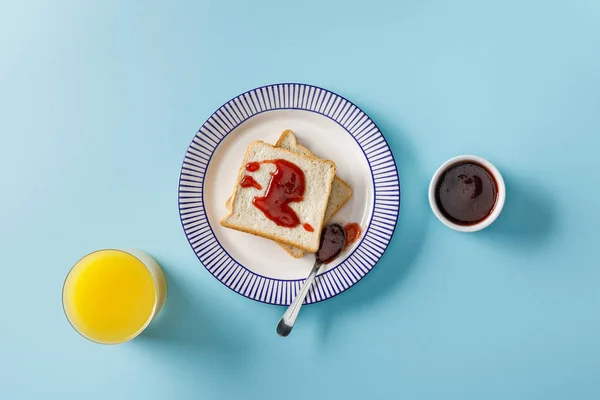 Vista superior de jugo de naranja, tostadas, tazón y cuchara con mermelada en placa ornamental sobre fondo azul - foto de stock