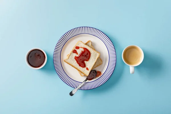 Vista superior de tostadas, cuchara, tazón con mermelada y taza de café sobre fondo azul - foto de stock
