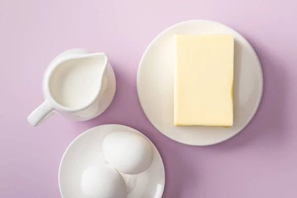 Draufsicht auf Butter, Milchkrug und gekochte Eier auf weißen Tellern auf violettem Hintergrund — Stockfoto