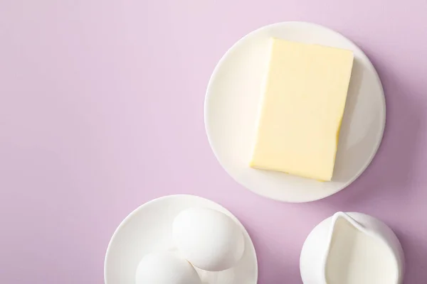 Вид сверху на масло, молоко и вареные яйца на белых тарелках на фиолетовом фоне — стоковое фото