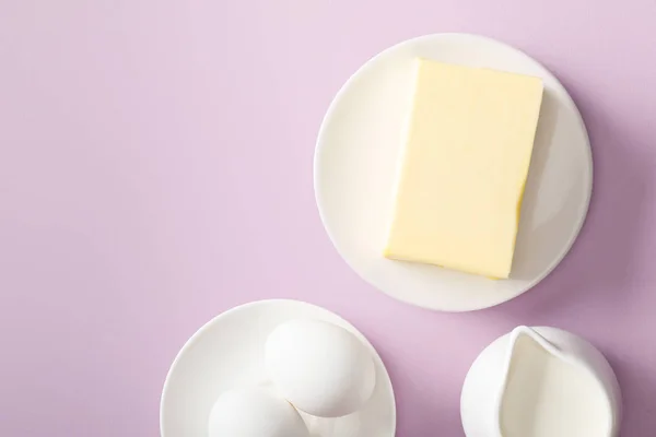 Top view of butter, milk and boiled eggs on white plates on violet background — Stock Photo