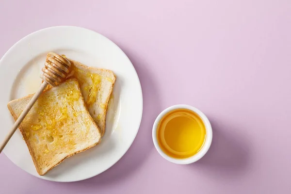 Vista dall'alto della ciotola, pane tostato con miele su piatto bianco e paletta di legno su sfondo viola — Foto stock