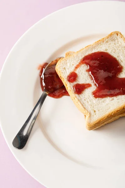Vista ravvicinata di pani tostati e cucchiaio con marmellata su piatto bianco isolato su viola — Foto stock