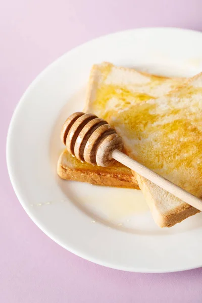 Close up view of toasts with honey and wooden dipper on white plate on violet background — Stock Photo