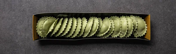 Top view of green raw ravioli in cardboard box on grey textured surface, panoramic shot — Stock Photo