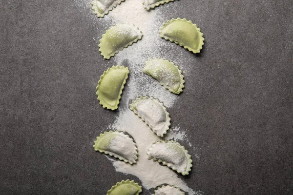 Vista superior de ravioli verde cru com farinha espalhada na superfície texturizada cinza — Fotografia de Stock