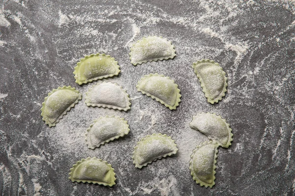 Vista superior de ravioles verdes crudos con harina en superficie texturizada gris - foto de stock