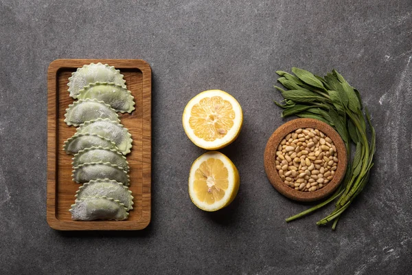 Serviti su tavola di legno ravioli verdi con farina vicino ciotola con semi, metà limone ed erbe aromatiche — Foto stock
