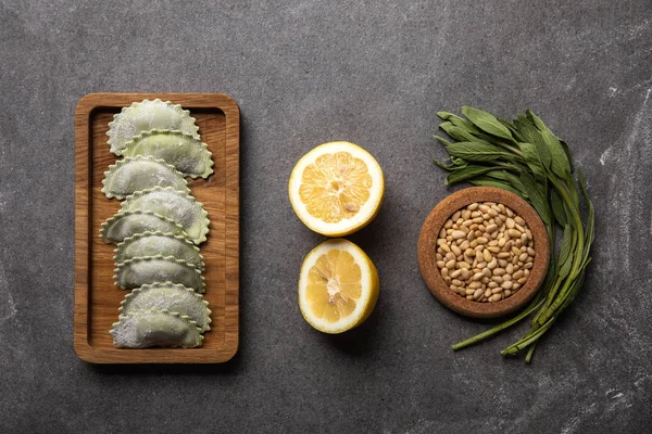 Served on wooden board green ravioli with flour near bowl with seeds, lemon halves and herb — Stock Photo