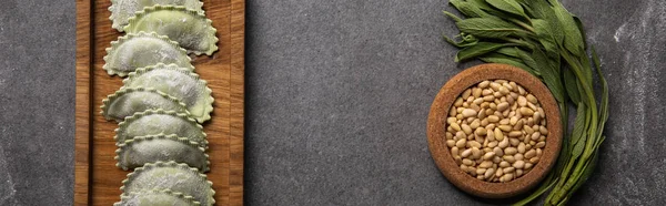 Servito su tavola di legno ravioli verdi con farina vicino ciotola con semi ed erbe aromatiche, colpo panoramico — Foto stock