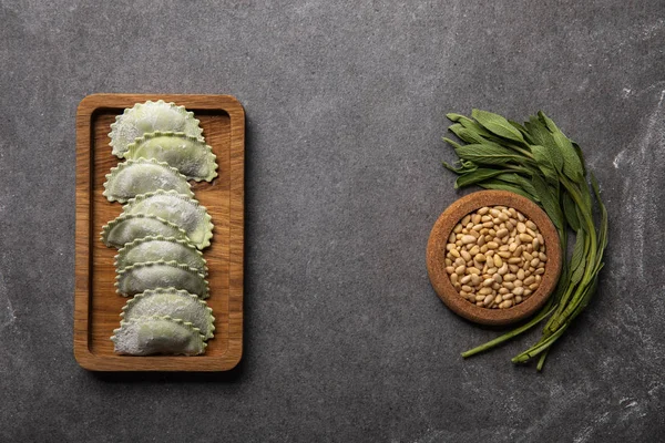 Servi sur une planche de bois raviolis verts avec de la farine près du bol avec des graines et des herbes — Photo de stock