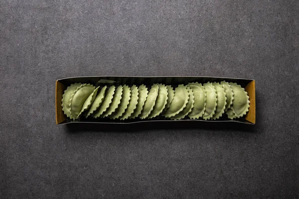 Vista superior de ravioli verde cru em caixa de papelão na superfície texturizada cinza — Fotografia de Stock