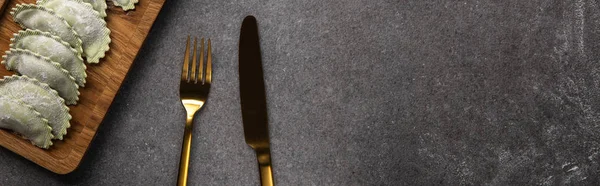 Servi sur une planche de bois raviolis verts près des couverts sur fond gris avec espace de copie, vue panoramique — Photo de stock