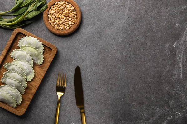 Serviti su tavola di legno ravioli verdi con farina vicino ciotola con semi, erbe e posate — Foto stock