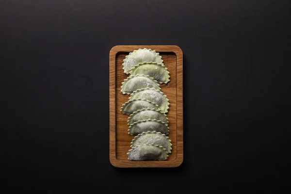 Top view of raw green ravioli with flour on wooden board isolated on black — Stock Photo