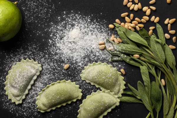 Green raw ravioli, pine nuts, herb, lime and flour on black background — Stock Photo