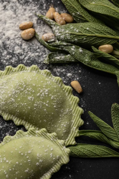 Close up view of green ravioli, sage and pine nuts on black table — Stock Photo