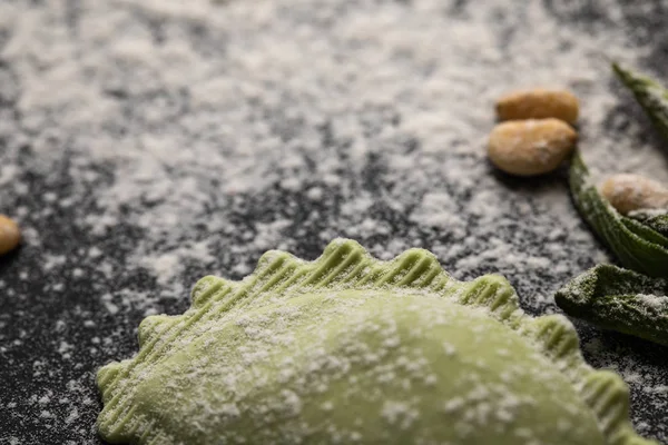 Selective focus of green ravioli and scattered flour on black table — Stock Photo